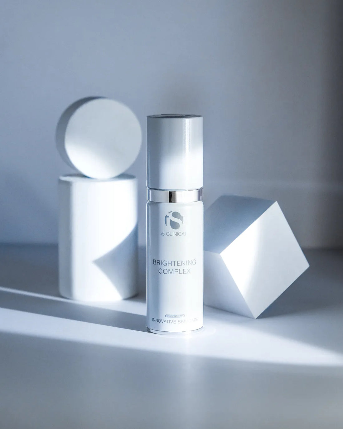 iS Clinical Brightening Complex bottle with silver cap among white geometric shapes