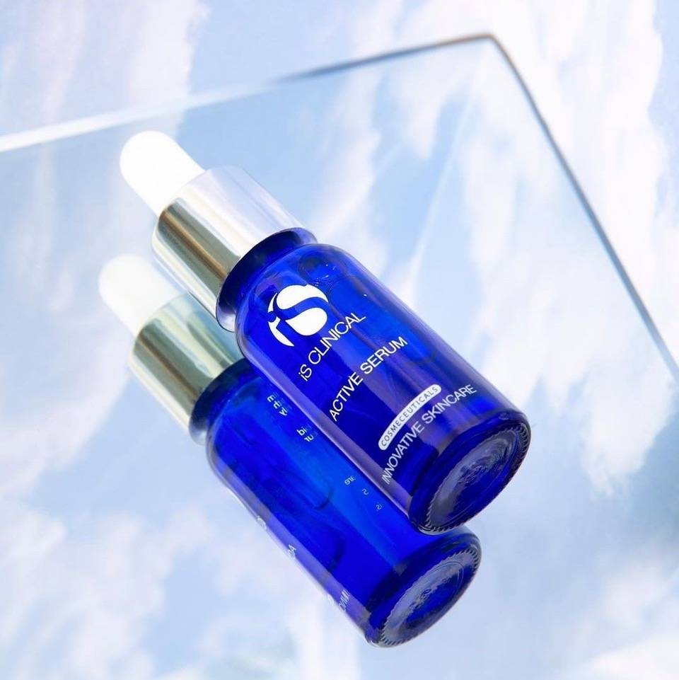 Blue glass bottle of iS Clinical Active Serum with silver dropper cap reflected on a glossy surface