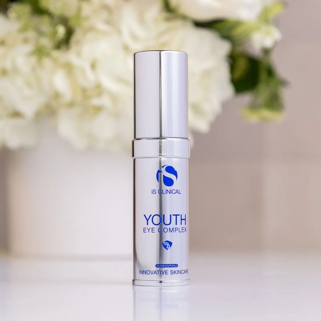 Silver pump bottle of iS Clinical Youth Eye Complex with blurred white flowers in background