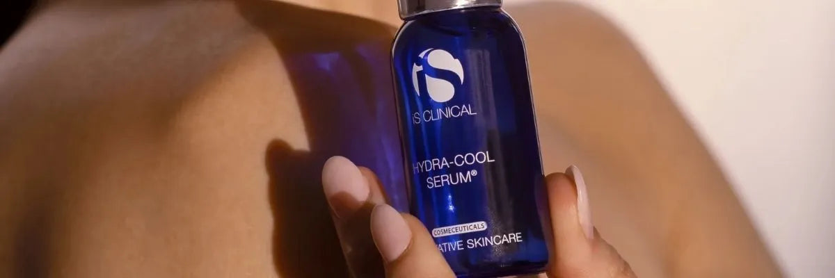 Hand holding iS Clinical Hydra-Cool Serum blue bottle against bare shoulder background