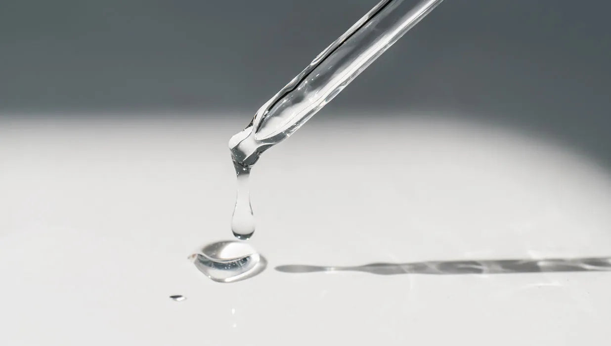 Clear serum drop falling from glass dropper onto white surface with soft shadow
