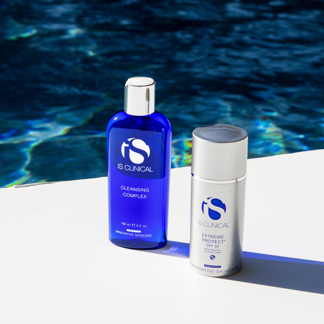 iS Clinical Cleansing Complex blue bottle and Extreme Protect SPF 30 white bottle on white surface by water