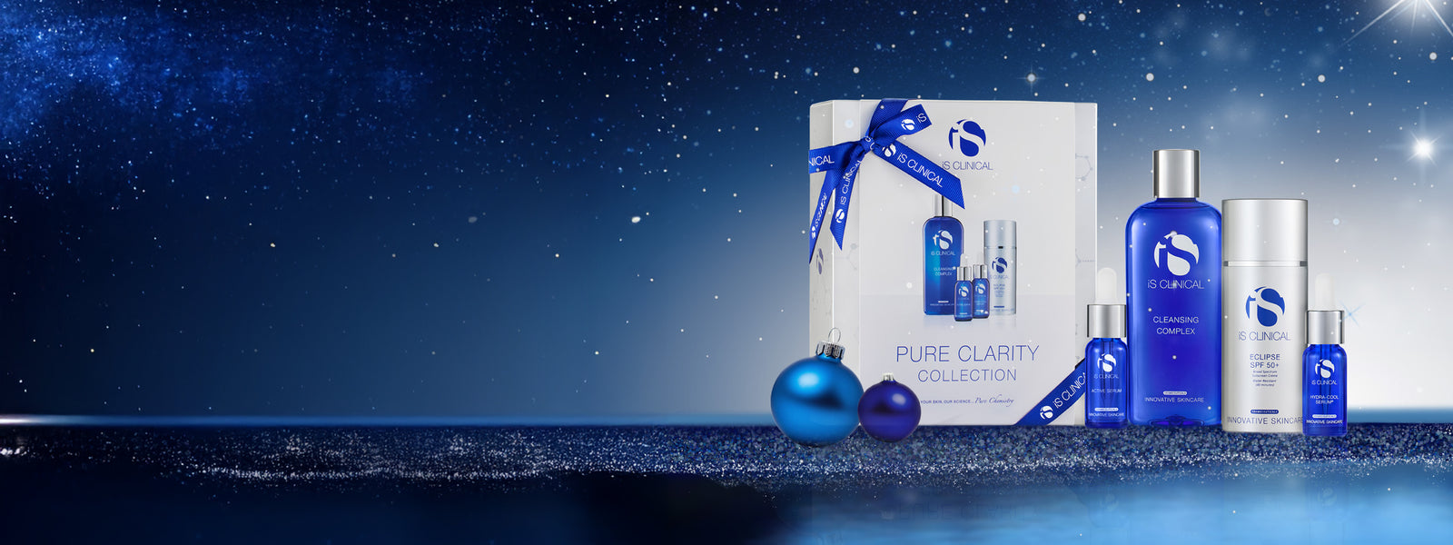iS Clinical Pure Clarity Collection gift box with blue ribbon, surrounded by blue and silver skincare bottles and blue festive baubles on a starry night background