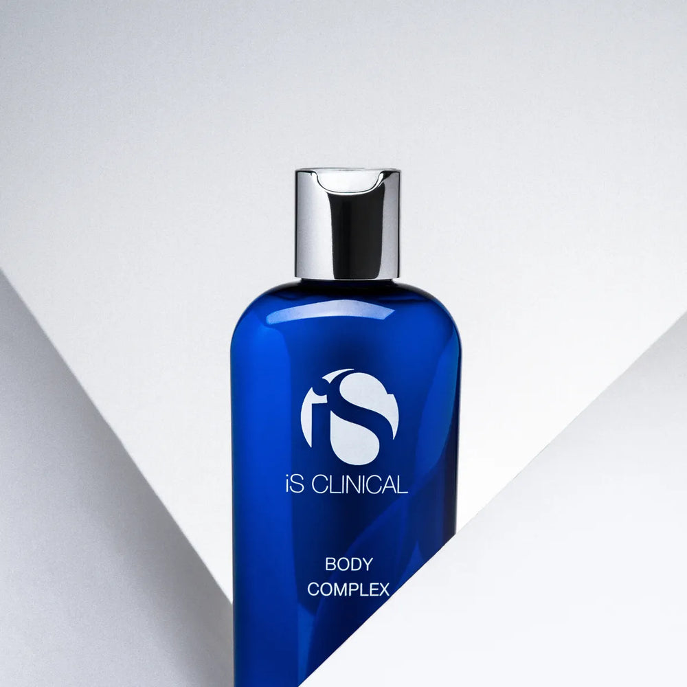 Blue bottle of iS Clinical Body Complex with silver cap against white geometric background