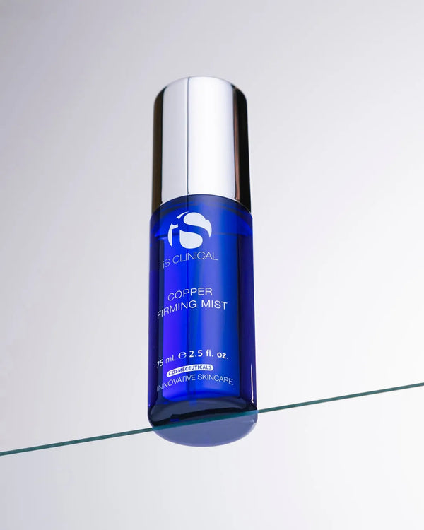 Blue cylindrical bottle of iS Clinical Copper Firming Mist with silver cap on glass surface
