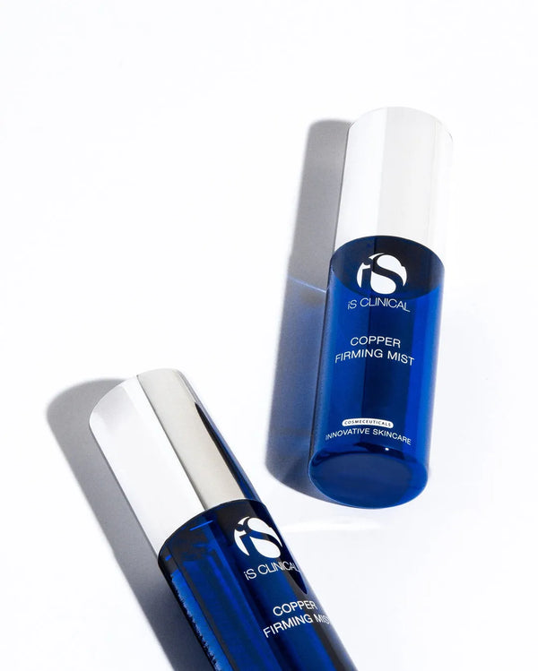 Two blue cylindrical bottles of iS Clinical Copper Firming Mist with silver caps on white background