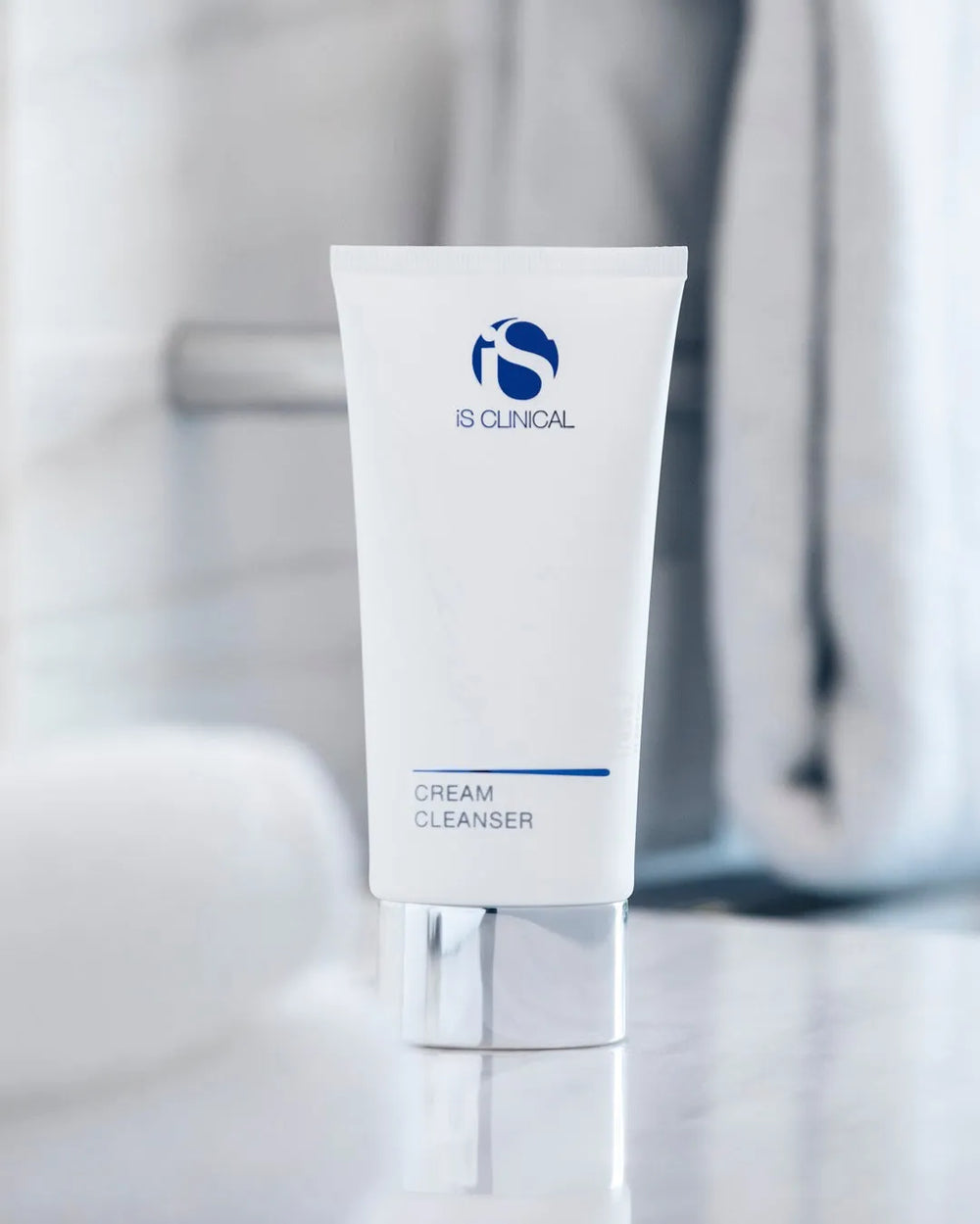 White tube of iS Clinical Cream Cleanser with silver cap on reflective surface, blurred background