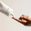 White tube of iS Clinical Cream Cleanser dispensing white cream onto fingertip against neutral background