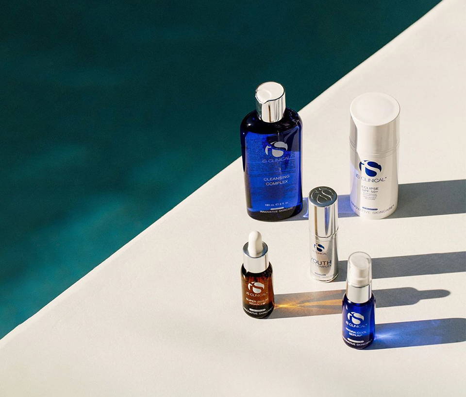 Five iS Clinical products incl. Cleansing Complex and Hydra-Cool Serum beside a pool
