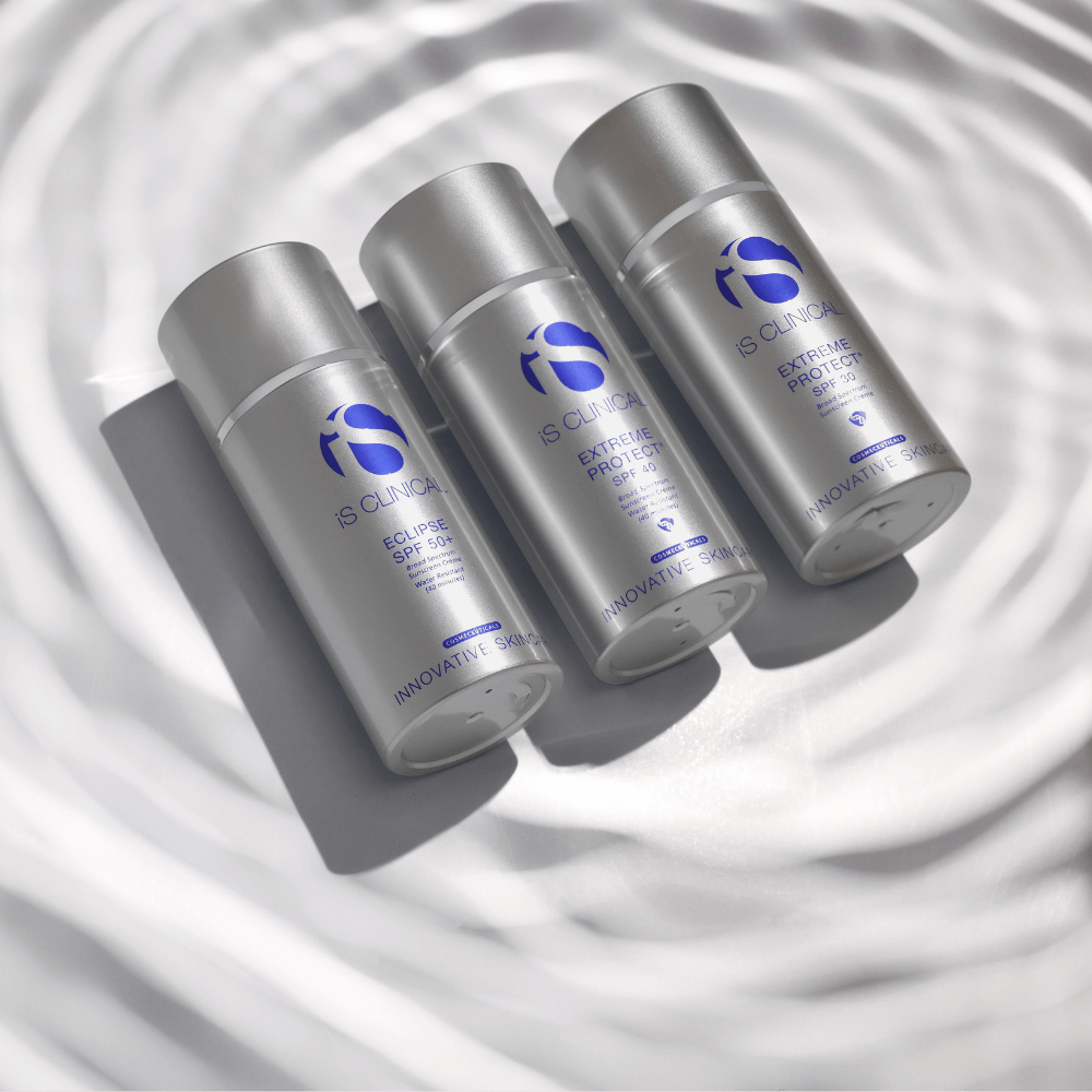Three silver iS Clinical sunscreen bottles labelled Eclipse SPF 50+, Extreme Protect SPF 40, and Extreme Protect SPF 30 on rippled white surface