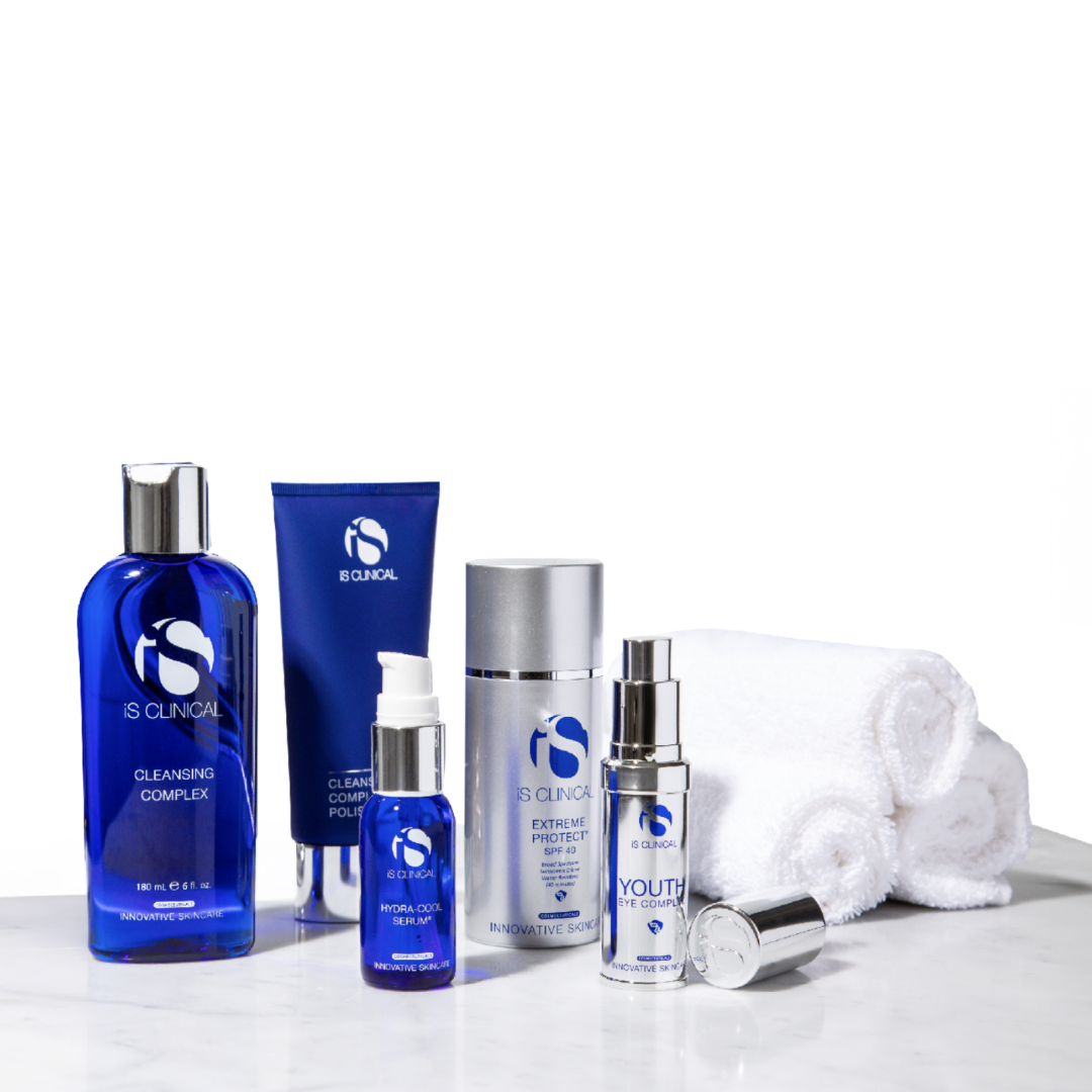 Five iS Clinical skincare products including Cleansing Complex, Hydra-Cool Serum, Extreme Protect SPF 40, Youth Eye Complex, and Cleansing Complex Polish with three rolled white towels