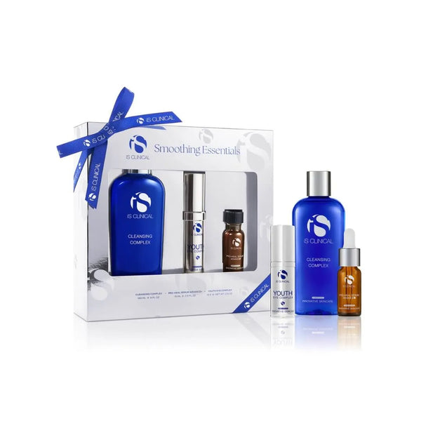 iS Clinical Limited Edition Smoothing Essentials set with Cleansing Complex, Youth Eye Complex, and Pro-Heal Serum Advance+ in blue and brown bottles with white and silver packaging