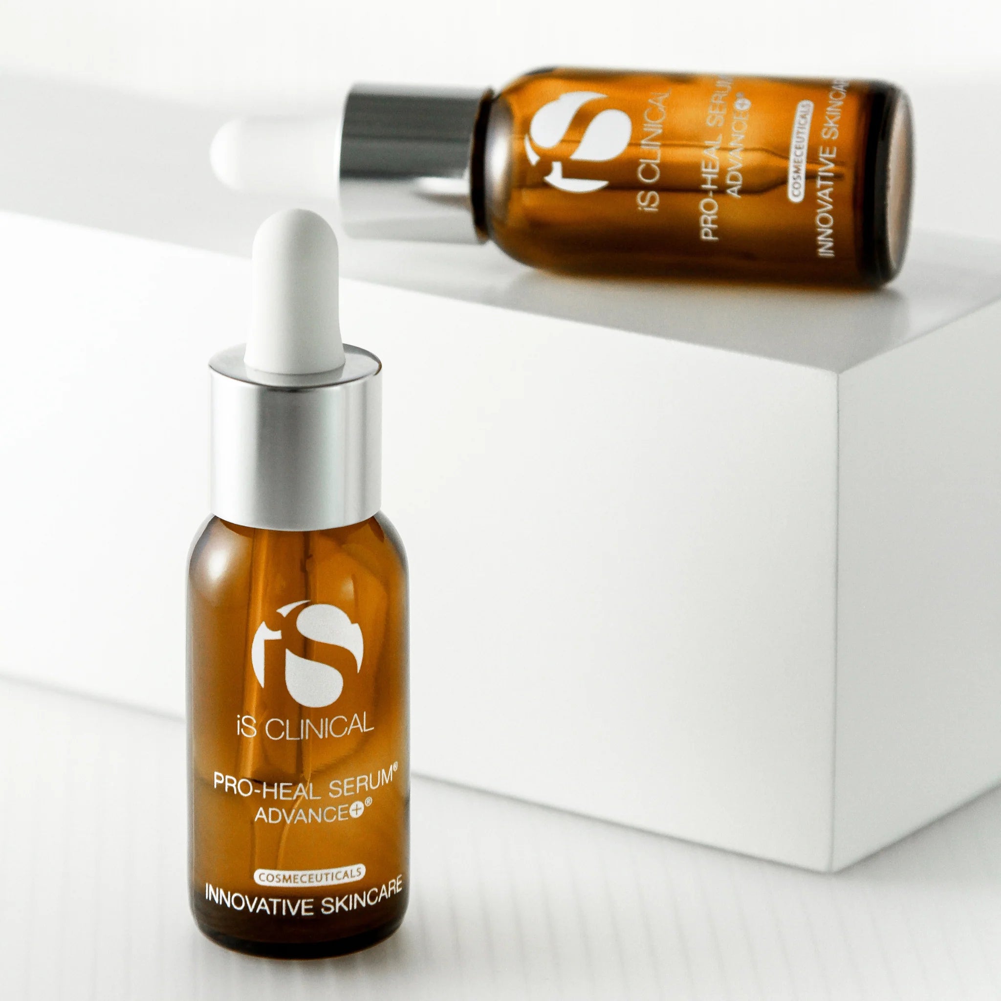 Two amber glass dropper bottles of iS Clinical Pro-Heal Serum Advance+ on white surfaces