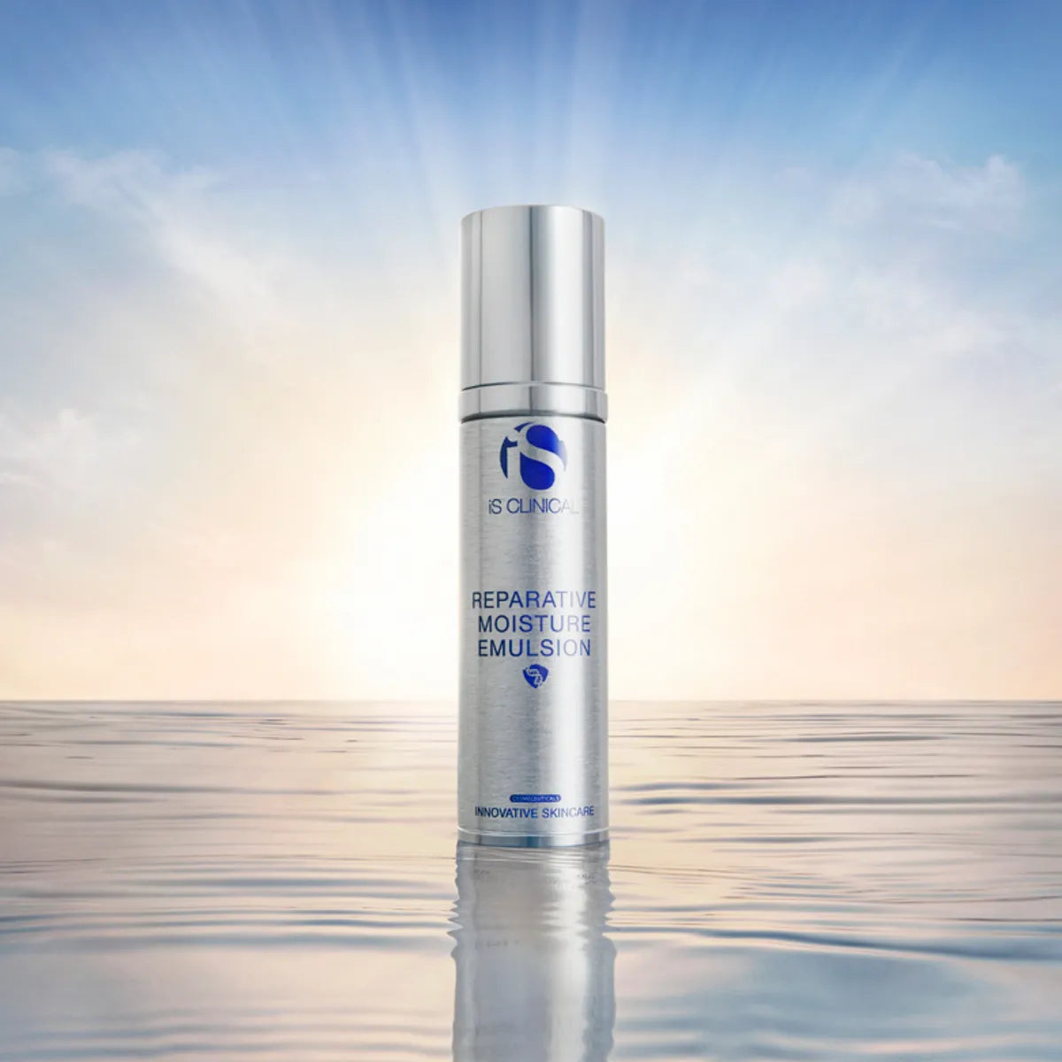Silver bottle of iS Clinical Reparative Moisture Emulsion 50g standing on reflective water surface with sunrise background