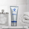 Silver tube of iS Clinical SHEALD Recovery Balm with blue text on marble surface, blurred towel and dispenser background
