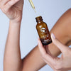 Hand holding amber glass bottle of iS Clinical Super Serum Advance+ with dropper releasing serum drop