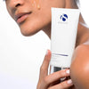 Close-up of a person holding iS Clinical Warming Honey Cleanser tube with honey-coloured cleanser on cheek