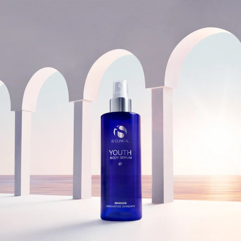 Blue pump bottle of iS Clinical Youth Body Serum with white arches and ocean background
