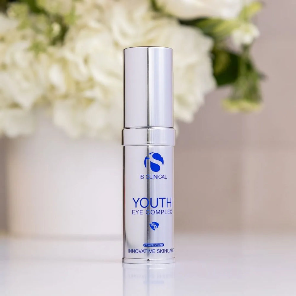 Silver pump bottle of iS Clinical Youth Eye Complex with blurred white flowers in background