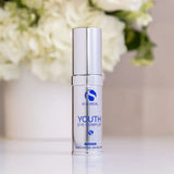 Silver pump bottle of iS Clinical Youth Eye Complex with blurred white flowers in background