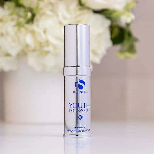Silver pump bottle of iS Clinical Youth Eye Complex with blurred white flowers in background