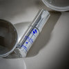 Silver cylindrical bottle of iS Clinical Youth Eye Complex with blue text on a reflective surface
