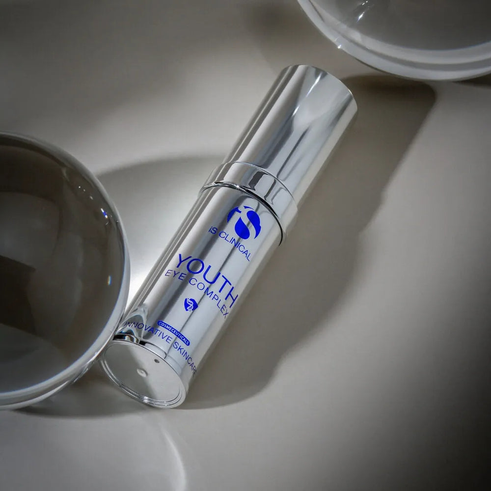 Silver cylindrical bottle of iS Clinical Youth Eye Complex with blue text on a reflective surface