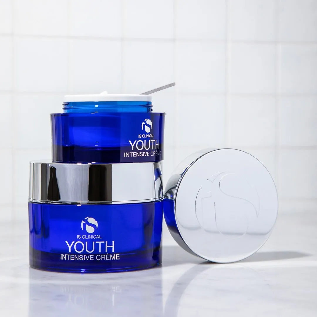 Two blue jars of iS Clinical Youth Intensive Crème, one open showing white cream and spatula