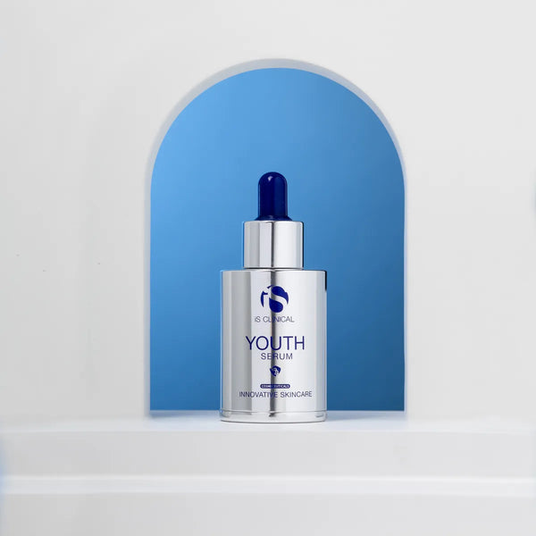 Silver bottle of iS Clinical Youth Serum with blue dropper cap against blue arched background