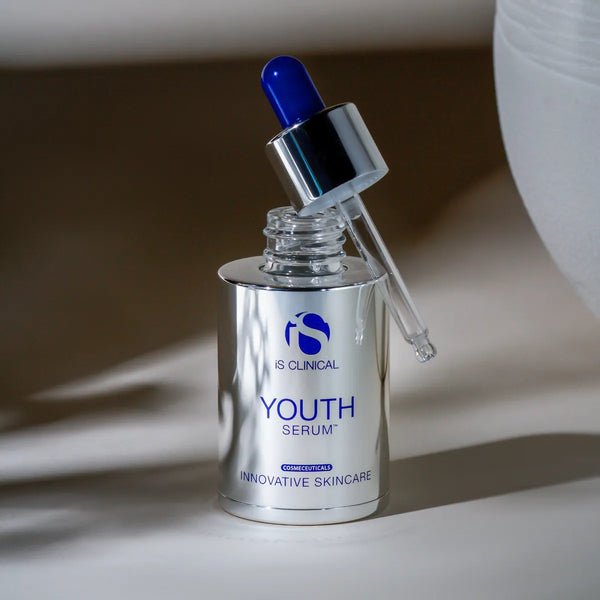 Silver bottle of iS Clinical Youth Serum with blue dropper cap and clear pipette on white surface